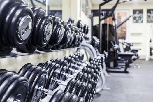 Black dumbbell set. Close up many rubberized dumbbells on rack in sport fitness center , Weight Training Equipment concept