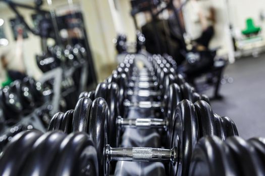 Black dumbbell set. Close up many rubberized dumbbells on rack in sport fitness center , Weight Training Equipment concept