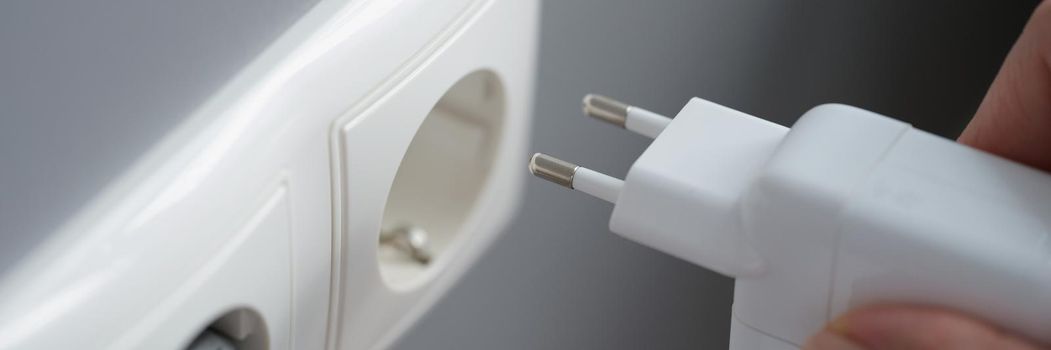 A female hand plugs the power supply unit for a laptop into an outlet, close-up. Uninterruptible power supply, phone charger