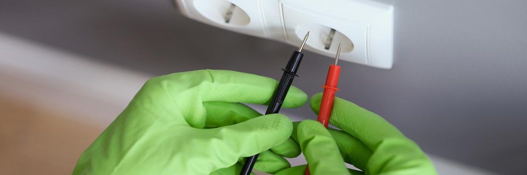 Measuring voltage with a multimeter, hands in rubber gloves close-up. Measuring instrument for electrical repair and maintenance