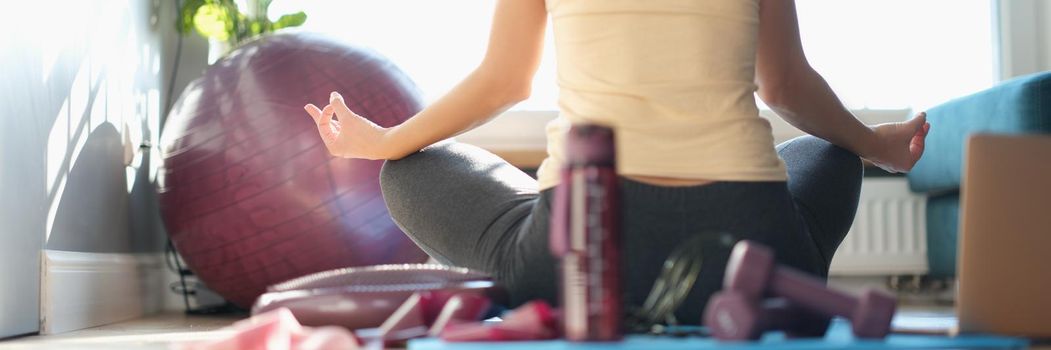 A woman sits in front of a window in a yoga pose, view from the back. Calm exercise, pandemic fatigue, self-isolation