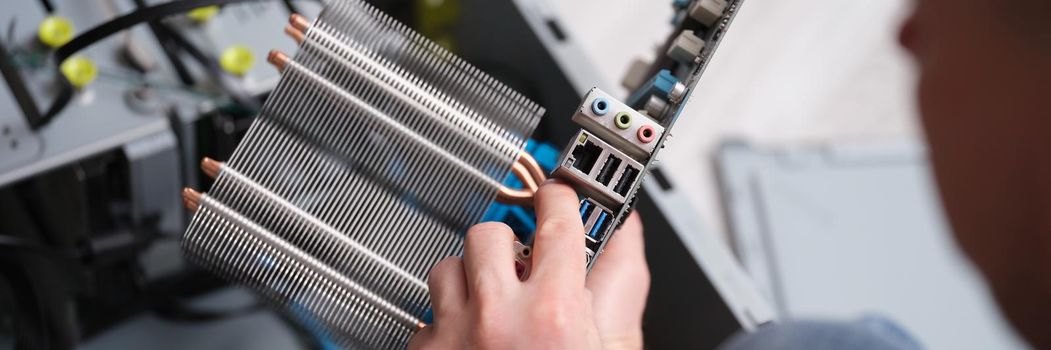 A man holds a motherboard, hands close-up. Repair and maintenance of electronics, replacement of computer components