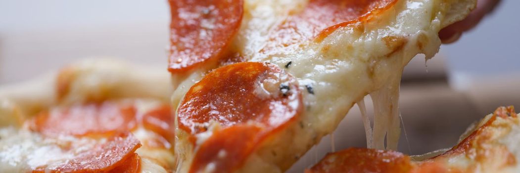 A man takes a large slice of hot neo-Politan pizza, close-up. Sausage with melted cheese on a flatbread, fast food