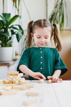 Little cute preschool girl plays at home with wood toys on table. Natural tactility development.