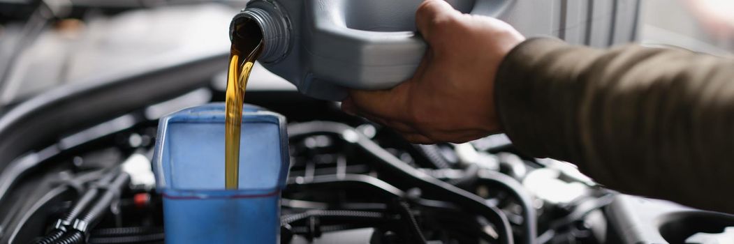 Male hands pouring machine oil from a canister into a car, close-up. Oil motor change, garage service