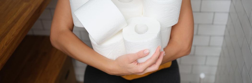 A woman is sitting on the toilet with rolls of toilet paper, close-up. Hygiene supplies during lockdown