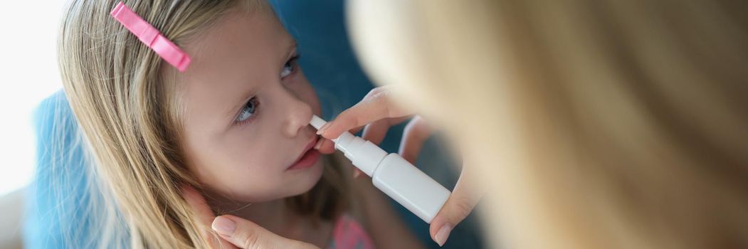 Mom sprays the baby's nose with a spray, the girl's face close-up. Prevention of drying out of the nasal mucosa, essential oils