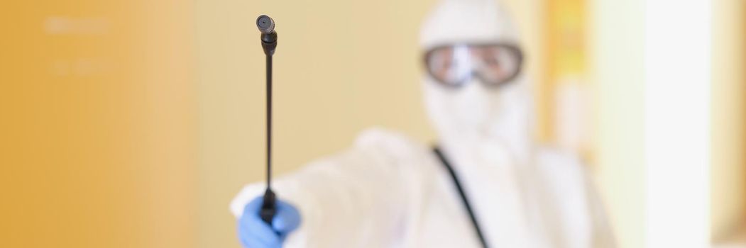 A man in a protective suit holds a sprayer, close-up, blurry. Equipment for high quality professional disinfection