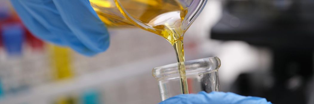 Yellow liquid is pouring into a measuring vessel, close-up. Checking the quality of engine oil, creating biofuels in the laboratory