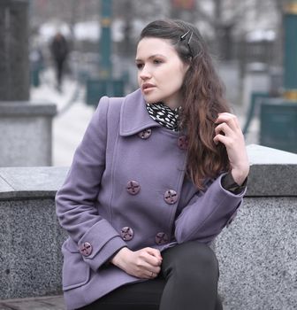 woman in fashionable coat sitting on bench in city.