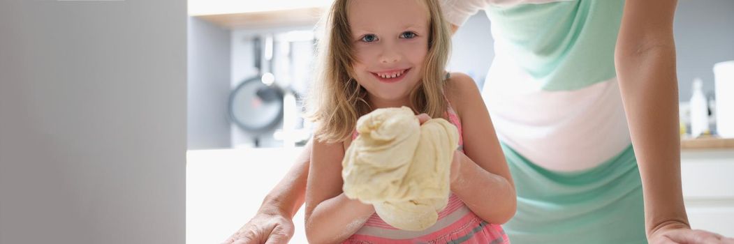 Little girl shows the dough and smiles, close-up. Raising children, mom devotes time to her daughter