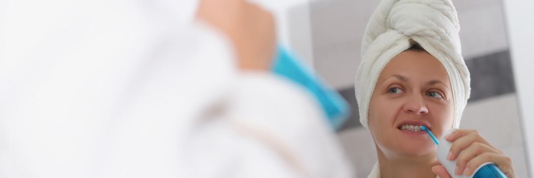 A woman is brushing her teeth with a modern device, close-up. Morning hygiene procedures at home or in the hotel