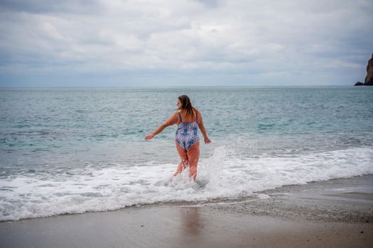 A plump woman in a bathing suit enters the water during the surf. Alone on the beach, Gray sky in the clouds, swimming in winter