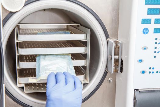 Nurse in latex glove is sterilizing bandages in autoclave. Horizontal sterilization system in dental office.