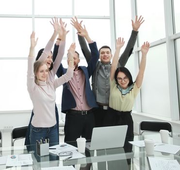 happy business team standing near the desktop with hands up. concept of success