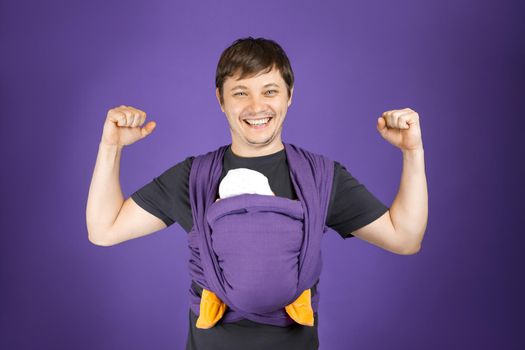 Young smiling father and baby in sling, front wrap carry. Happy fatherhood, free hand babywearing concept.