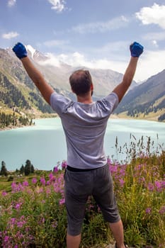 A man raised his hands to the sky next to a mountain lake. Spectacular scenic on Big Almaty Lake ,Tien-Shan Mountains in Almaty region of Kazakhstan. Vertical