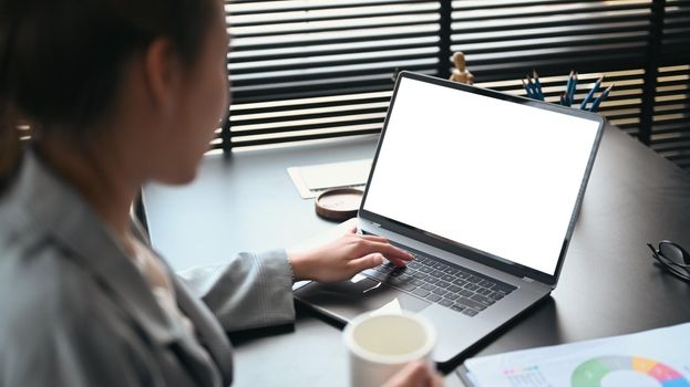 View over businesswoman shoulder working on laptop in her workstation.