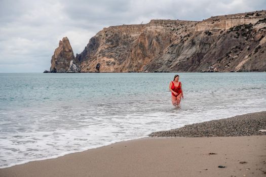 Woman in a bathing suit at the sea. A fat young woman in a red swimsuit enters the water during the surf.