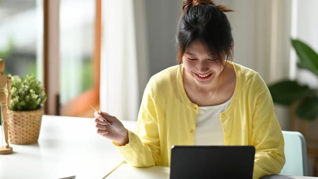 Happy asian woman shopping online, using internet banking service on computer tablet.