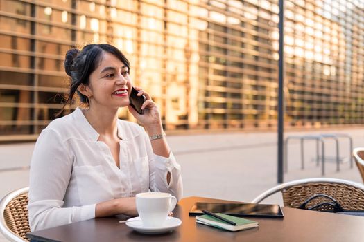 smiling businesswoman talking on the phone on the terrace of a coffee shop, concept of digital entrepreneur and urban lifestyle, copy space for text