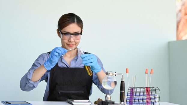 Shot of researcher putting dry sample of cannabis into flask and tubes with colorful substances on table. Herbal alternative medicine, cbd oil concept.