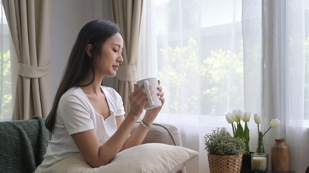 Satisfied young woman relaxing on couch and drinking hot coffee in the morning.