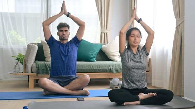 Peaceful young couple meditating, sitting in lotus position on mats. Healthy lifestyle, yoga, pilates, exercising concept.