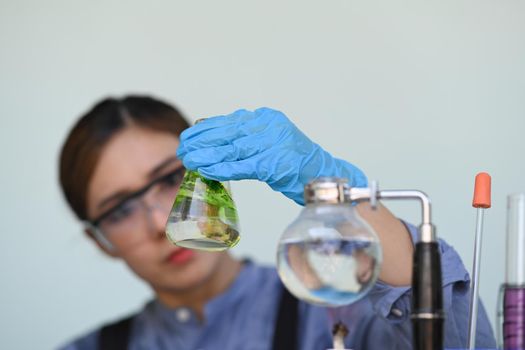 Scientist with glasses and gloves researching and examining hemp oil in laboratory. Herbal alternative medicine, cbd oil concept.