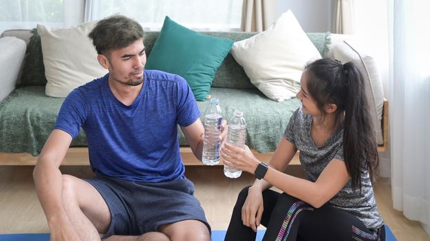 Joyful young couple in sportswear resting and drinking water after morning workout at home.