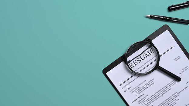 Top view resumes of applicants and magnifying glass on green background. Job search concept.