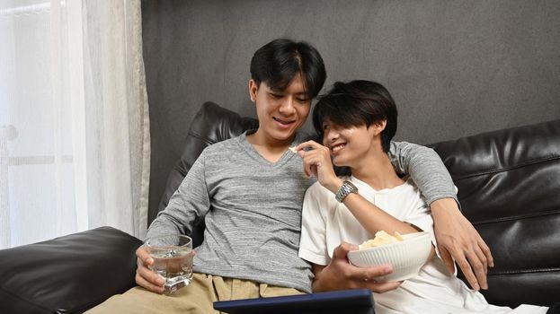 Young homosexual couple embracing and enjoying the movie on laptop. LGBT and love concept.