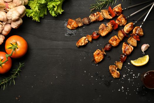 Delicious grilled meat skewers with with tomato, sweet pepper and onions on black wooden table. Top view with copy space.