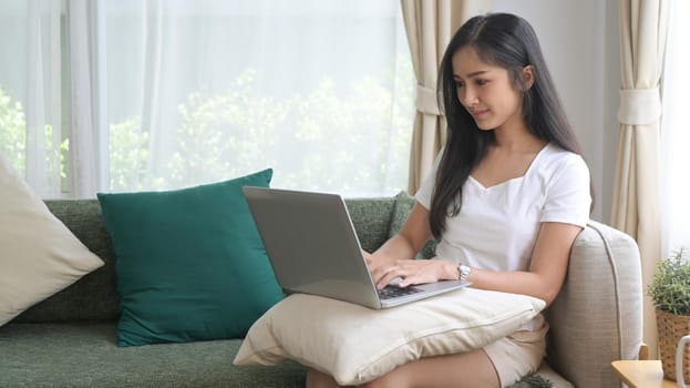 Beautiful asian woman in casual clothes resting on couch and using computer laptop.