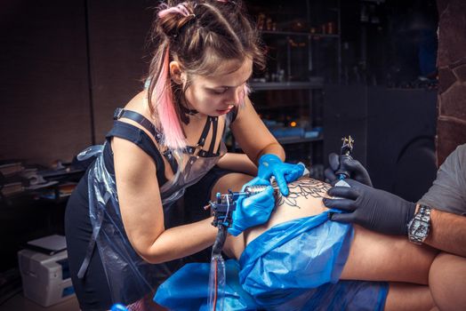 Tattoo specialist at work in tatoo salon./Tattoo artist does tattoo on the skin of his client in tattoo studio.
