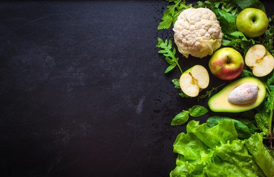 Fresh green vegetables and fruits on black chalk board background. Сauliflower, avocado, spinach, lettuce salad, green apples, herbs. Vegetarian food. Diet/healthy/detox food concept. Space for text