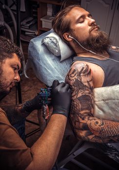 Tattooer doing tattoo in tattoo studio./Man wearing gloves posing in tatoo salon.
