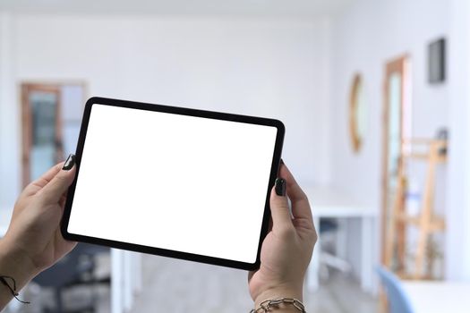 Mockup image of hands holding and showing digital tablet with blurred cafe background. Empty screen for graphic display montage.