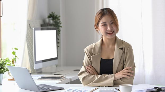 Pretty female employee sitting in modern office and smiling confidently to camera.