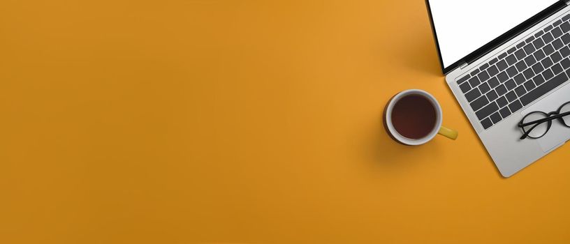 Computer laptop, coffee cup and glasses on yellow background with copy space for your information content.