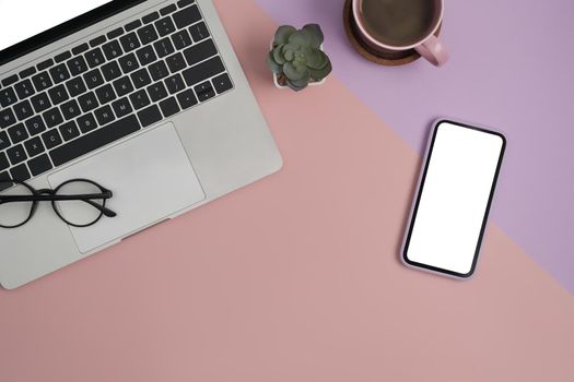Computer laptop, smart phone, glasses, coffee cup and notebook on modern feminine workplace. Top view.