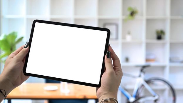 Stylish man hands holding mock up digital tablet with blurred home office background.