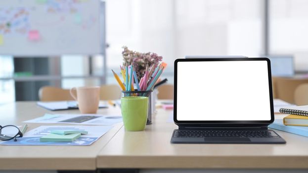 Digital tablet with wireless keyboard and supplies on wooden table at comfortable office.