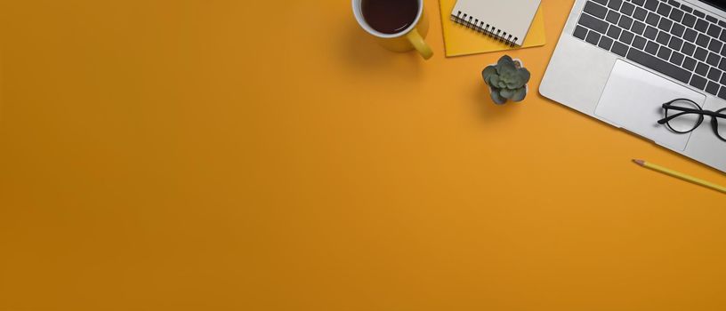 From above view laptop computer, notepads and coffee cup on yellow background with copy space.