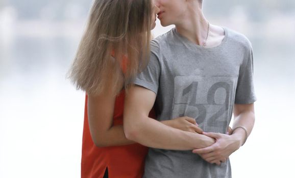 young couple kissing while standing on the shore of the city lake.