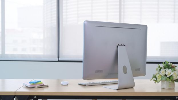 Modern workplace with computer pc, potted plant and sticky notes on wooden table.