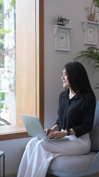 Thoughtful female entrepreneur sitting with laptop computer and looking through a window.