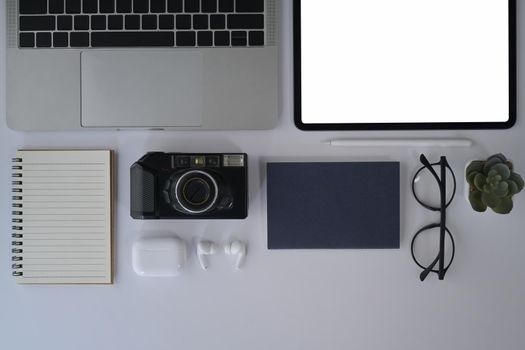 Flat lay designer workplace with digital tablet, camera, laptop, notebook and glasses.