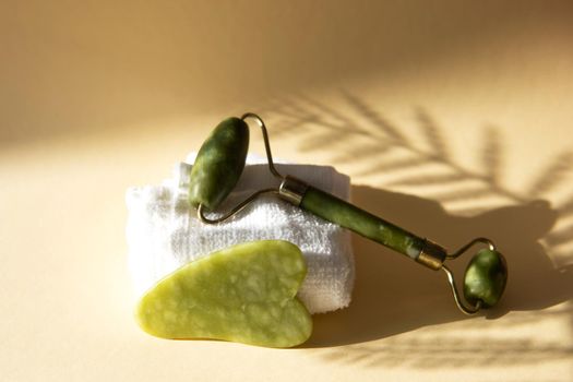 Jade Gua sha scraper and facial massager on beige background. Hard light, shadows, the concept self-care. Facial care. Zero waste. Lifting and toning treatment at home.