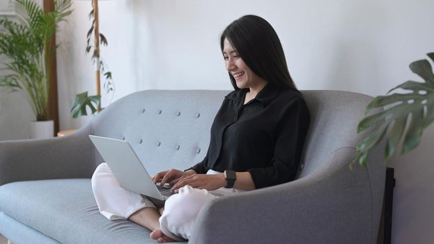 Smiling young woman freelancer working from home, surfing on internet on laptop computer.